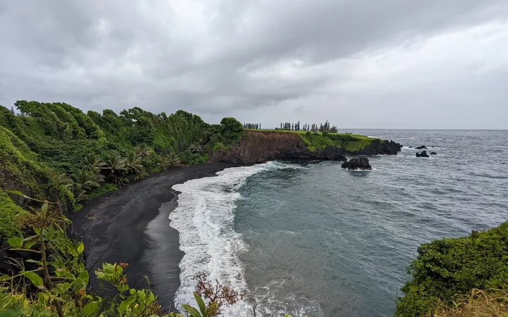 Black sand beach on Maui's Hana coast, framed by lush cliffs and turquoise surf